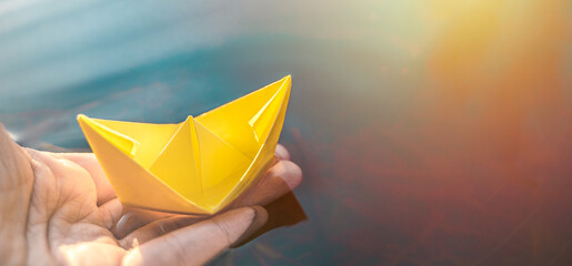 Yellow lonely floating paper boat in hand. Colorful sailing ship in big blue spring puddle, river...