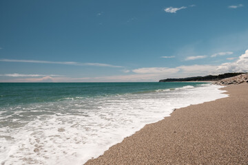 Blue water of the Tasman Sea lapping onto the sand at Maori Beach near Bruce Bay on the west coast of the South Island of New Zealand with forest in the distance