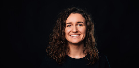 Fototapeta premium Banner size portrait of a wide smiling brunette woman over dark black background.