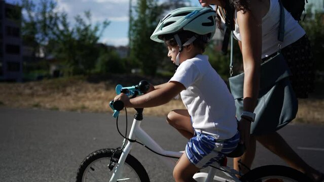 Active little boy learning to ride bicycle outside in sunny day with mother. Child learns to ride bike with the help of parent during sunny day