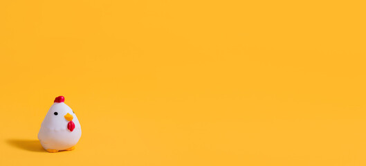 Rubber toy rooster on a yellow background. Children's background. Children's toy. Banner. Copy space. Place for text.