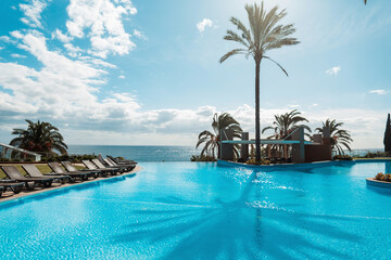 Beautiful summer exotic ocean view with swimming pool, palm trees, blue sky and sunbeds in Madeira...