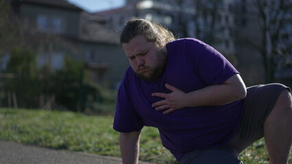 Person having heart attack outdoors. An overweight young man suffering from chest pain unable to breath having to sit down