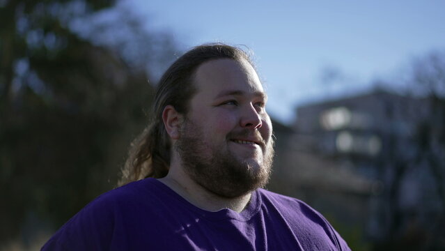One pensive happy young man walking forward outside smiling. A joyful overweight guy walks outdoors feeling positive. Tracking shot