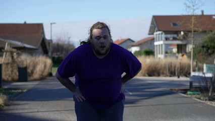 Fototapeta premium One exhausted overweight young man having chest pains standing outside. A fat male person having heart pulpitations recovering breath standing outside