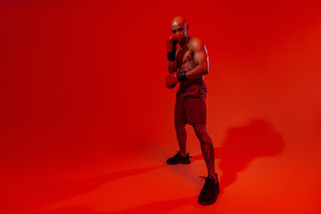Fototapeta na wymiar Sporty man wearing boxing gloves practicing for fight on studio background. Strength and motivation
