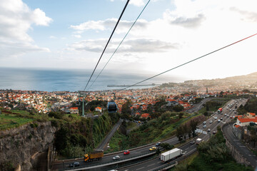 Fototapeta na wymiar Beautiful view of Funchal city with road and cars, ocean at sunset. Cable car ride over the city in Madeira island