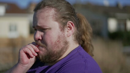 Fototapeta premium Concerned young man standing outdoors feeling anxiety. Closeup face tracking shot on overweight male person with preoccupied expression