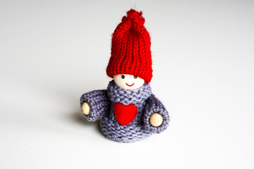 A small smiling wooden doll boy with a red knitted hat and a red heart on his chest