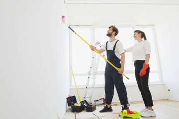 Young attractive couple makes repairs in apartment and paint walls in white color. Family apartment renovation concept