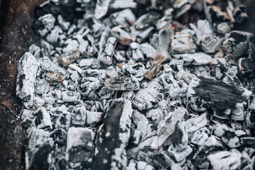 Photo of smoldering gray coals, burnt ash close-up in a fire.