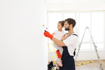 Repair in the apartment. Happy family father and daughter paint the wall with white paint. Daddy...