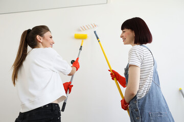 Back view of beautiful young caucasian happy women makes repairs in apartment while painting interior wall with paint rollers in new house. Home decoration concept.