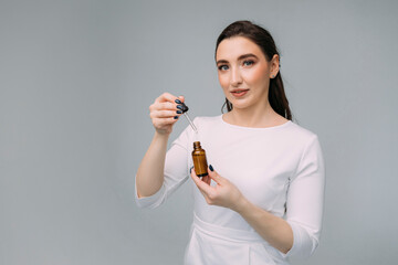 young girl doctor in a white dressing gown holds a pipette and a glass bottle with serum in her hands. Woman in a cosmetology clinic, hyaluronic acid, anti-aging therapy