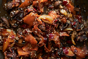 Fototapeta premium fried mushrooms with carrots and onions, sprinkled with sesame seeds. close-up of fried mushrooms with carrots and onions, sesame seeds