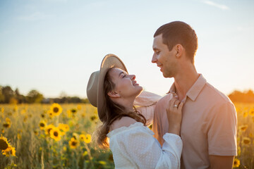 Young beautiful couple in love in a sunflower field at sunset. Summer.