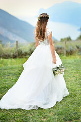  Bride in a white dress stands, holding her bouquet behind her back