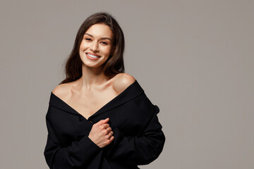 Beautiful stylish smiling girl in blue jeans and black jacket sitting on a chair on a gray background. The concept of lightness and femininity, fashion.