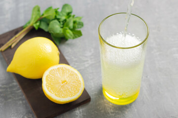 Pouring lemonade or carbonated soda drink into a glass, lemon fruit and mint leaves, refreshing summer beverage