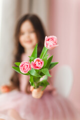 Portrait of a little girl with long dark hair close-up. The baby hugs a bouquet of fresh, delicate pink tulips. A gift for the holiday, spring time.
