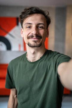 One man young adult caucasian male standing at home with brown hair mustaches and beard looking to the camera happy smile confident real people green t shirt UGC selfie user generated content