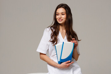 A beautiful young cosmetologist doctor in a white medical suit smiles at the camera and holds cosmetology products in her hands. Self care, beauty and cosmetology concept.