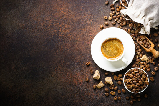 Cup of coffee, roasted coffee beans and sugar at dark table . Top view image with copy space.