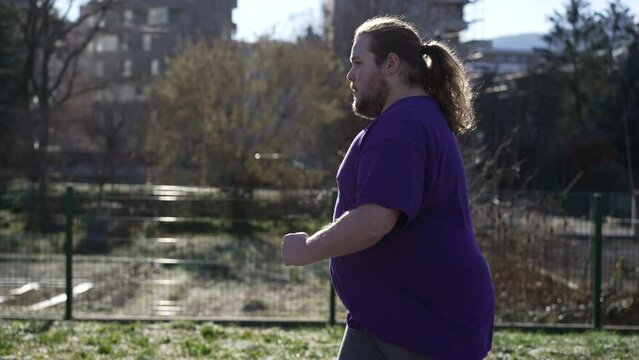 One young determined overweight man running outdoors. A fat person getting back into fitness. Profile close up tracking shot. Motivational sport concept