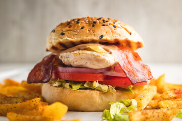 Delicious grilled chicken sandwich with onion rings, tomato and bacon, served with French fries.