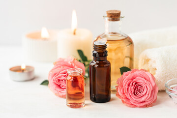 Obraz na płótnie Canvas Aromatherapy. Concept of pure organic essential rose oil. Elixir with plant based floral or herbal ingredients. Pink flowers extract. Spa atmosphere with candle, towel. White background