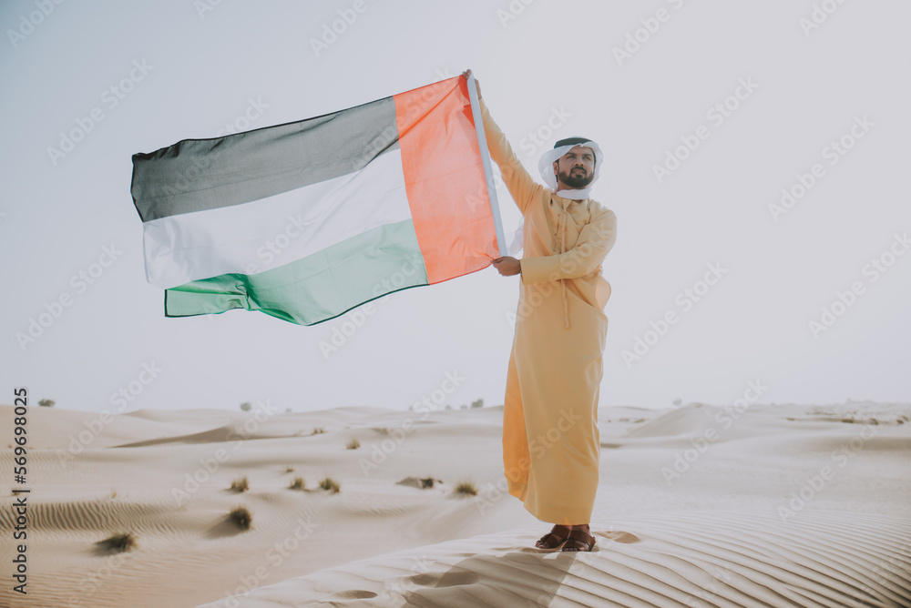 Wall mural Man wearing traditional uae clothes spending time in the desert