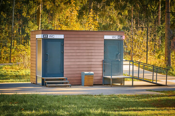 Public toilet in park. Wooden WC building in fall forest in park. Modern outdoor public toilet in...