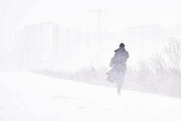 silhouette of a man walking in a snowstorm in the city the concept of a storm blizzard and bad weather. - obrazy, fototapety, plakaty