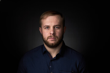 Portrait of a young confident blonde in a dark shirt, with a beard on a dark background