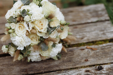 A wedding bouquet of white roses lies on old wooden boards. Wooden texture and green moss. Wedding rings.