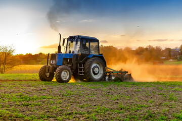 Modern blue tractor machinery plowing agricultural field meadow at farm at spring autumn during sunset.Farmer cultivating,make soil tillage before seeding plants,crops,nature countryside rural scene