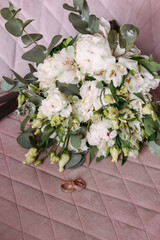 A wedding bouquet of white roses lies on old wooden boards. Wooden texture and green moss. Wedding rings.