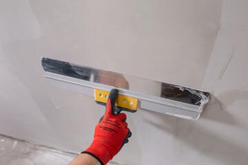 A professional finisher painter levels the walls with putty with a wide spatula - wall decoration for wallpaper and painting