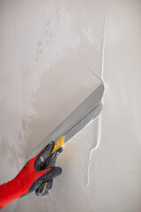 A professional finisher painter levels the walls with putty with a wide spatula - wall decoration for wallpaper and painting