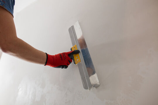 A professional finisher painter levels the walls with putty with a wide spatula - wall decoration for wallpaper and painting