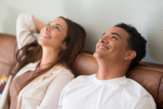 Happy Young Couple Dreaming Together Looking Up At Home Their Future. Couple Dream Future. Young Beautiful Loving Couple Relaxing On Sofa Together, Happy Millennial Family Sitting On Couch On Cozy