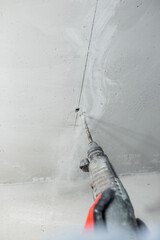 Builder electrician makes a hole puncher in a concrete wall for installation of electrical cables -...