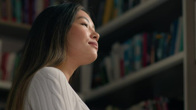 Young korean woman student looking with contemplation at bookshelf in university library in search right textbook concentrated girl in bookstore chooses books from bookcase selects literature to read