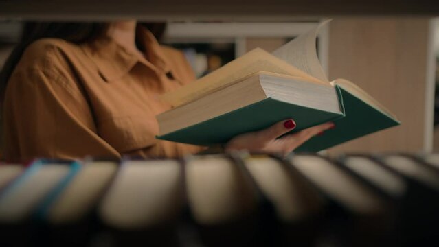 Close-up unrecognizable woman reading book in library female student teacher standing near bookshelf turning page textbook reads fiction preparing for university exam studying next to shelves books