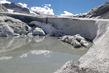 Close-up of melting  biggest glacier in Italian Alps, clouds in a sunny day, and reflections in the water, Adamello - Brenta Nature Park, Trentino, Italy.