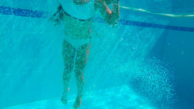 Little girl underwater jump in home pool. A funny child in nice swimsuit jumps under pool water in the sun rays.
