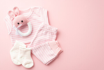 Baby shower concept. Top view photo of pink infant clothes shirt pants socks and knitted bunny rattle toy on isolated pastel pink background with blank space