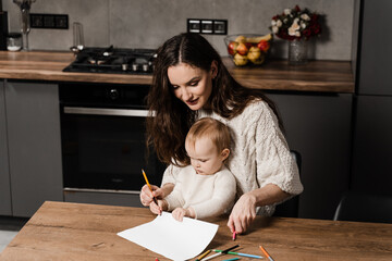 Mom and toddler daughter draw pictures with colored pencils and spend time with mother together. Developing drawing lesson for child toddler at home. Maternity leave.