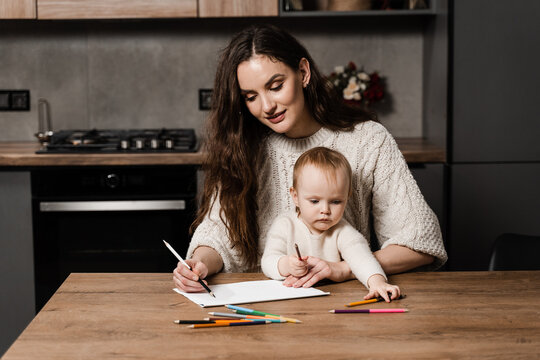 Mom and toddler daughter draw pictures with colored pencils and spend time with mother together. Developing drawing lesson for child toddler at home. Maternity leave.