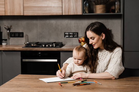 Mom and toddler daughter draw pictures with colored pencils and spend time with mother together. Developing drawing lesson for child toddler at home. Maternity leave.